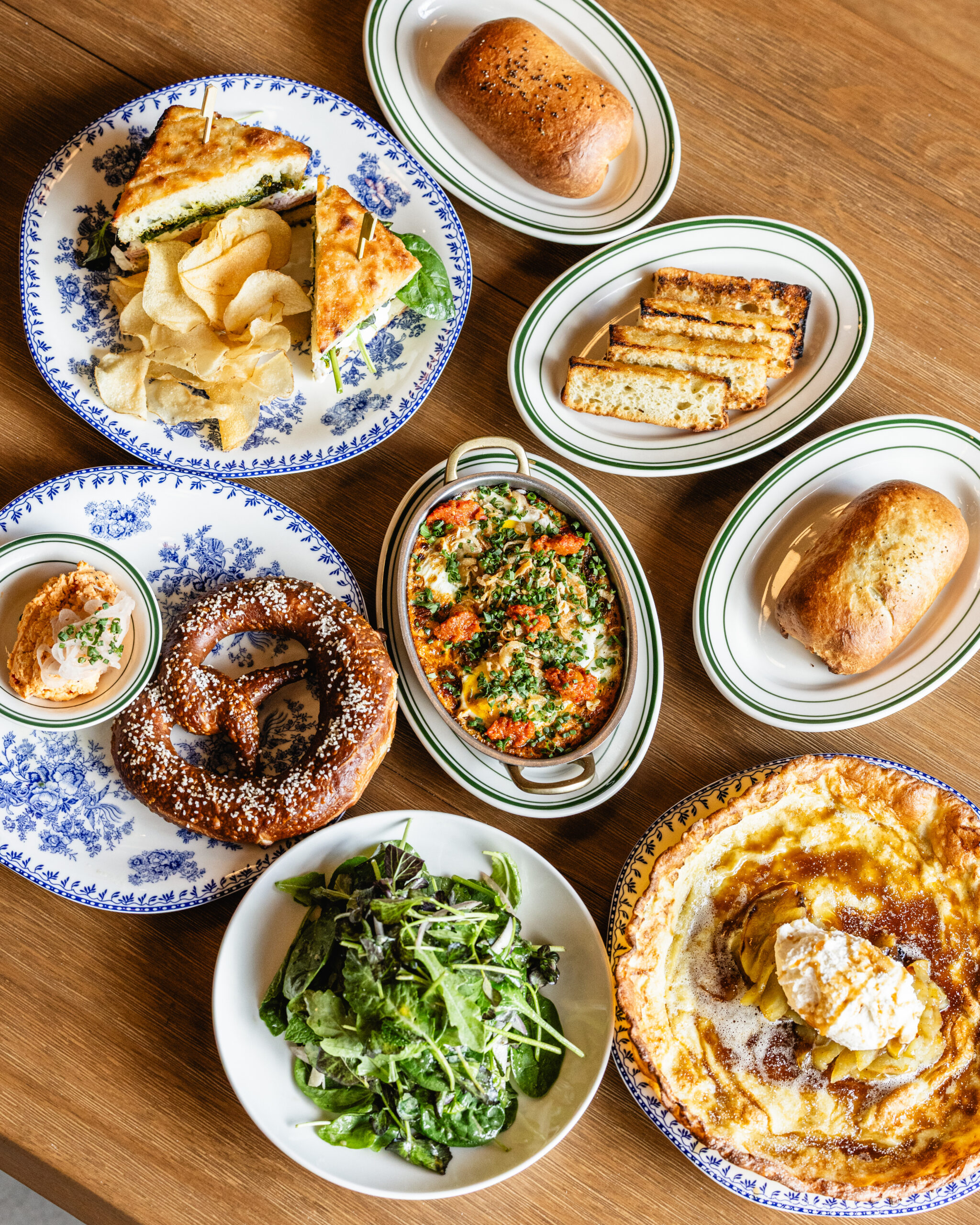 Overhead spread of Eckhart Beer Co. brunch dishes including pretzel, sandwich, salad, and dessert
