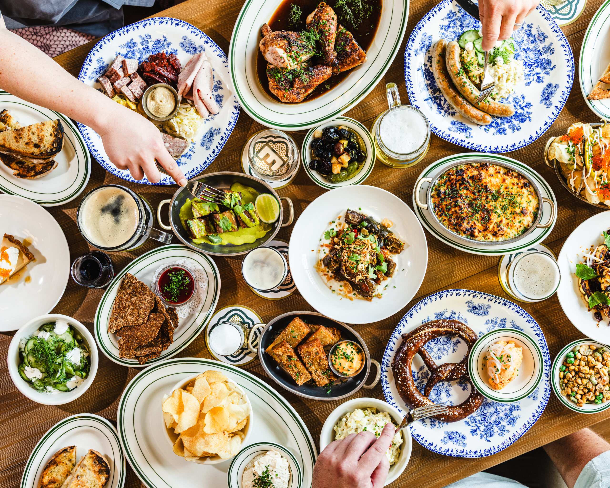 Overhead spread of Eckhart Beer Co. taproom dishes including sausages, roast chicken, pretzel, and beer