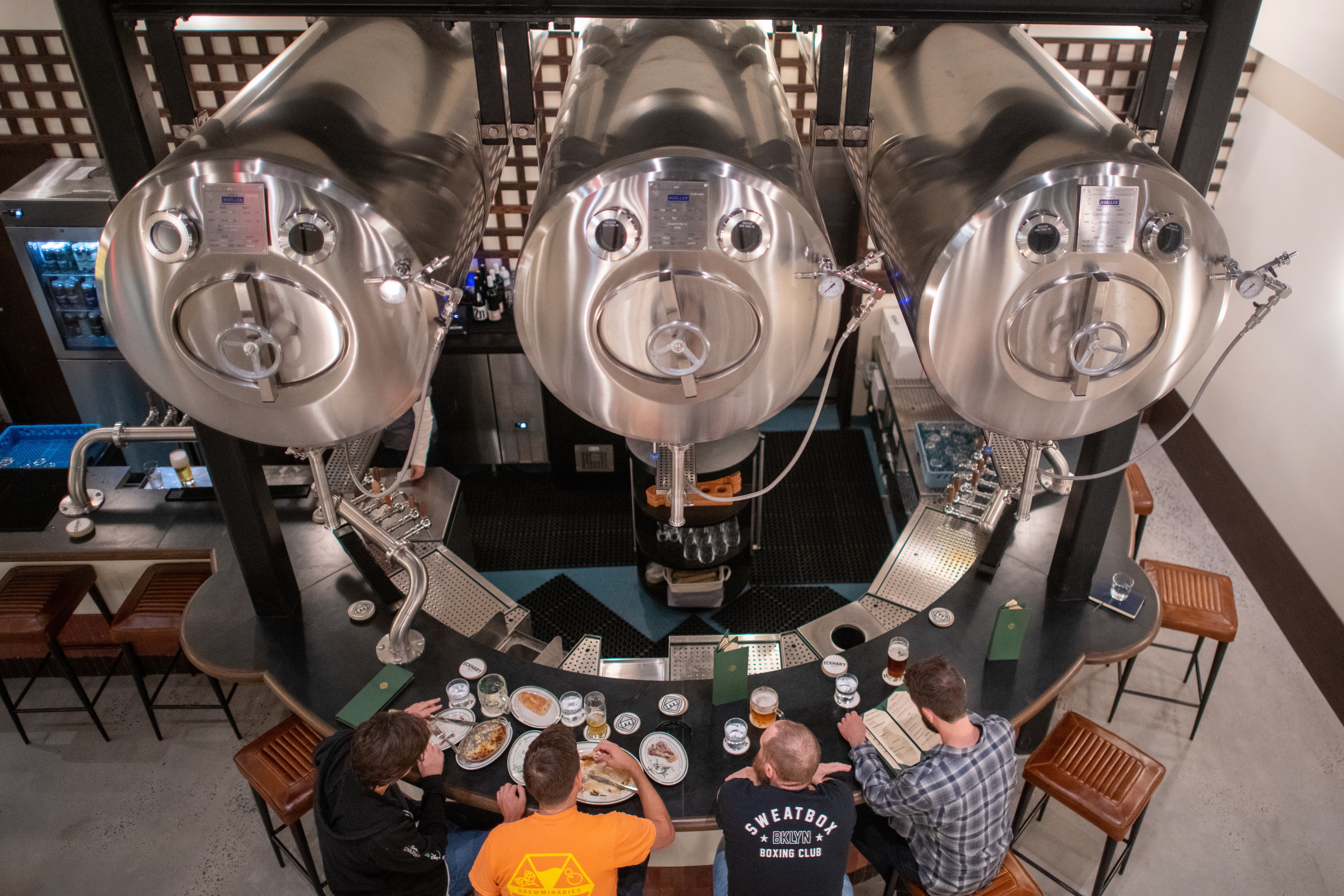 Overhead view of Eckhart Beer Co.'s taproom bar with fermentation tanks and guests enjoying drinks in Bushwick, Brooklyn